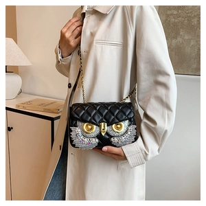 Detail of owl crossbody bag with rhinestone wings and gold chain on beige coat