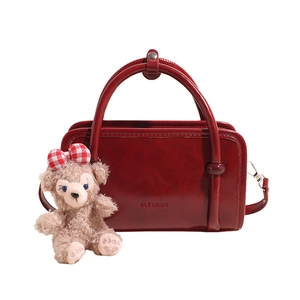 Retro red glossy handbag with round handle and plush bear charm in a frontal studio view