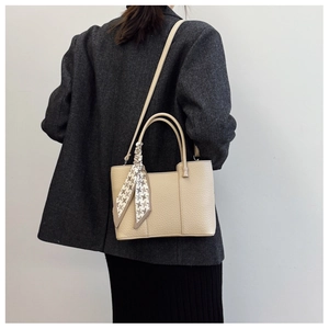 Detail view of beige lychee leather bucket bag featuring decorative silk scarf handle