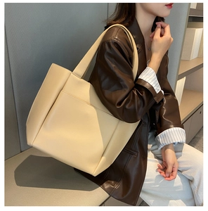 Close-up of a beige large-capacity tote bag with wide shoulder straps on a model