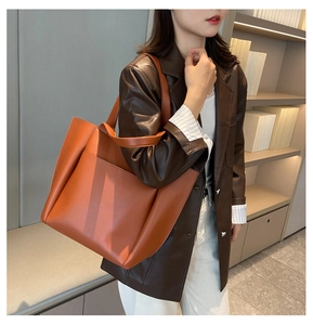 Brown leather tote bag shown on shoulder in a minimalist indoor library setting