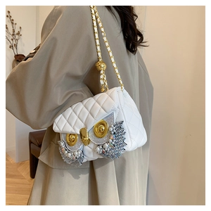 Detail of white quilted crossbody bag with owl decoration and golden chain strap