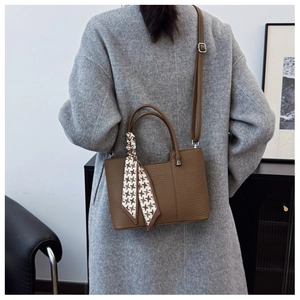 Close-up of brown litchi leather tote bag with houndstooth scarf on a model