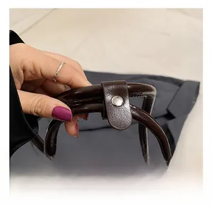 Detail of dark brown leather handle with metallic snap button and zipper closure
