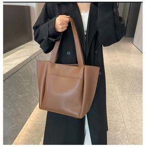 Detail of dark brown leather tote bag with front pocket shown on a model's shoulder