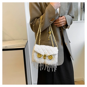 Detail of owl shaped white quilted bag with golden eyes and long beaded fringe tassels