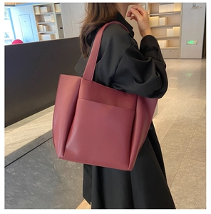 Burgundy red leather tote bag with wide shoulder strap shown in a lifestyle model shot
