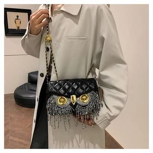 Detail of owl-shaped black quilted crossbody bag with golden eyes and crystal fringe