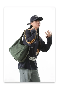 Détail d'un grand sac bandoulière en toile vert olive porté par un mannequin en tenue