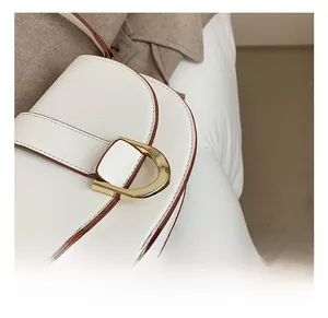 Détail d'un sac selle blanc montrant des bords marron et une boucle dorée en forme de D