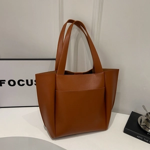 Large brown pebble grain leather tote bag for women shown on a minimalist white desk