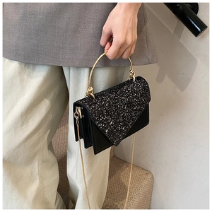 Detail of black sequined square bag with gold metal handle and chain strap on a model
