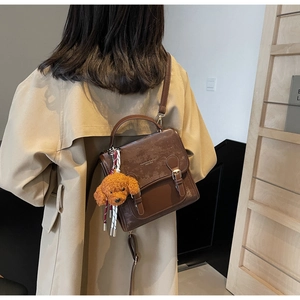 Borsa a tracolla retrò in pelle marrone con ciondolo a cane di peluche su trench beige