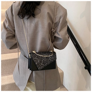 Detail of a black mini square bag with shiny sequins and a curved gold handle
