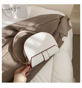Gros plan d'un sac selle blanc avec bordure marron et boucles métalliques dorées