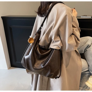 Detailed view of large dark brown leather tote bag with embossed fashion logo and woven charm