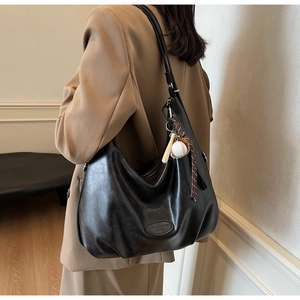 Detail of black leather hobo bag featuring a decorative baseball and bat charm pendant