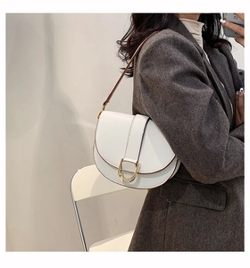 Gros plan d'un sac selle blanc avec boucle en D dorée porté sur un blazer gris