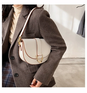 Détail d'un sac selle beige avec bords marrons et fermoir doré en U porté par un modèle