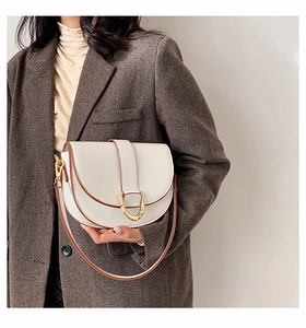 Gros plan d'un sac selle blanc avec boucle dorée porté sur un blazer marron