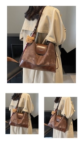 Detail of vintage brown tote bag with plush bear charm and silk scarf on a beige coat