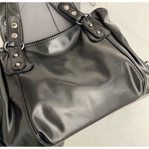 Détail d'un sac cabas en cuir noir avec clous argentés et larges anses bandoulières