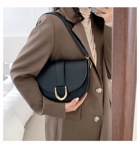 Selfie miroir montrant un sac selle en cuir noir avec boucle en métal doré à l'épaule
