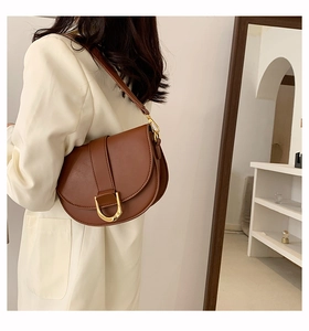Vue détaillée d'un sac besace marron foncé avec boucle en D dorée sur un blazer