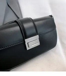 Close-up of sleek black leather square bag featuring a polished silver metal buckle clasp
