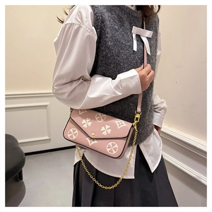 Pink crossbody bag featuring white floral patterns and a gold chain strap on model