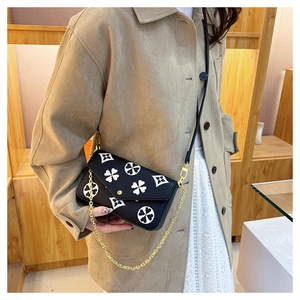 Detail view of black cross-body bag with white clover print and gold chain strap
