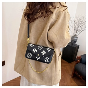 Detail view of the black crossbody bag with white floral print and golden chain strap