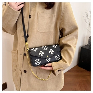 Detail of black textured leather crossbody bag featuring white clover pattern and gold buckle