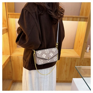 Detail of grey crossbody bag with clover pattern and gold chain strap worn by model