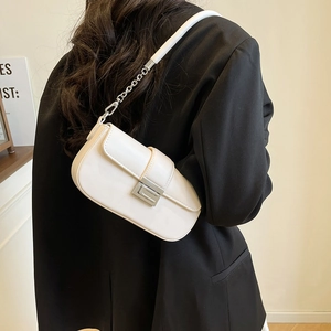 Detail of minimalist cream baguette bag with silver buckle and chain strap on a blazer