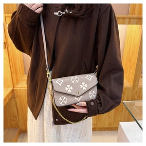 Close-up of a lilac envelope crossbody bag with clover pattern and gold chain strap