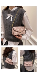 Close-up of pink leather envelope bag with white floral pattern and gold chain strap