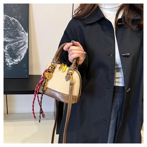 Detail of a mini beige shell bag with contrast trim and golden heart pendant