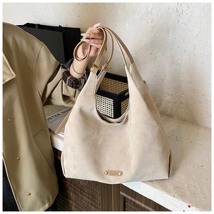 Detail of beige frosted leather tote bag showing soft texture and oval leather plaque