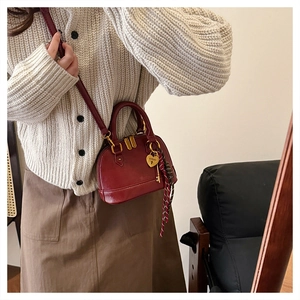 Detail of burgundy shell-shaped handbag with gold heart pendant and plaid ribbon scarf