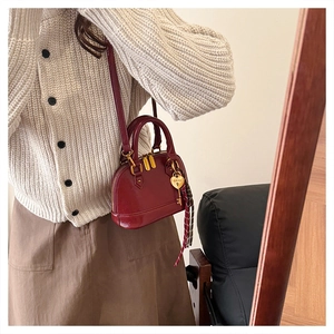 Detail of burgundy shell-shaped crossbody bag with gold heart pendant and plaid tassel