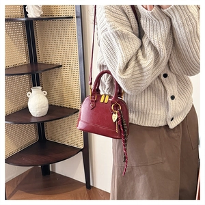 Detail of burgundy shell-shaped crossbody bag with gold hardware and silk scarf