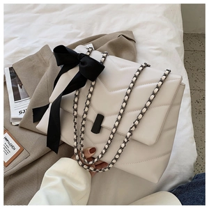 Detalle de bolso tote crema acolchado con lazo negro y correa de cadena metálica