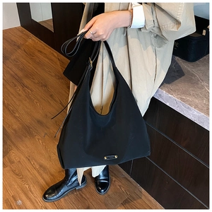 Detail of black large-capacity tote bag with golden metal logo and wide shoulder strap
