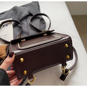 Detailed close-up of deep chocolate leather bag featuring gold-tone protective bottom studs
