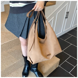 Close-up of matte camel leather tote bag featuring thin brown straps and metal logo detail