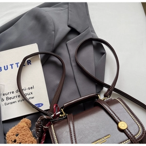 Detailed top view of a dark brown leather crossbody bag with a plush bear charm on a blazer
