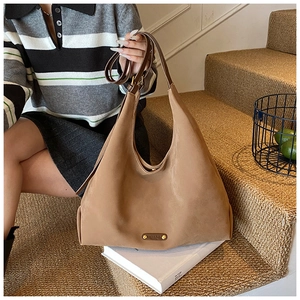 Close-up of brown suede hobo bag with adjustable strap and metal logo on book