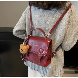 Detail of reddish-brown leather backpack with top handle and plush bear charm on a model