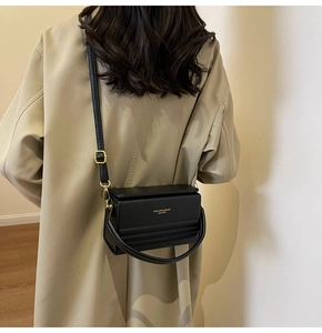 Detail of black box crossbody bag with gold buckle and adjustable strap on a trench coat
